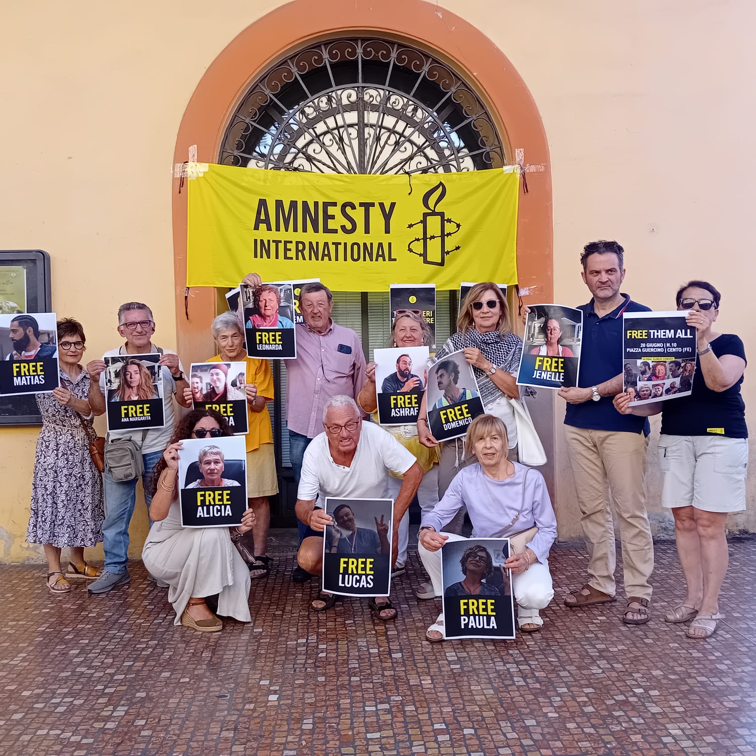 Gruppo di persone davanti a una chiesa con striscione Amnesty International e cartelli “FREE” per prigionieri.